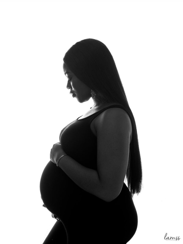 A black and white silhouette portrait of a pregnant woman in profile against a bright background. — portrait photography London by Lamss Media